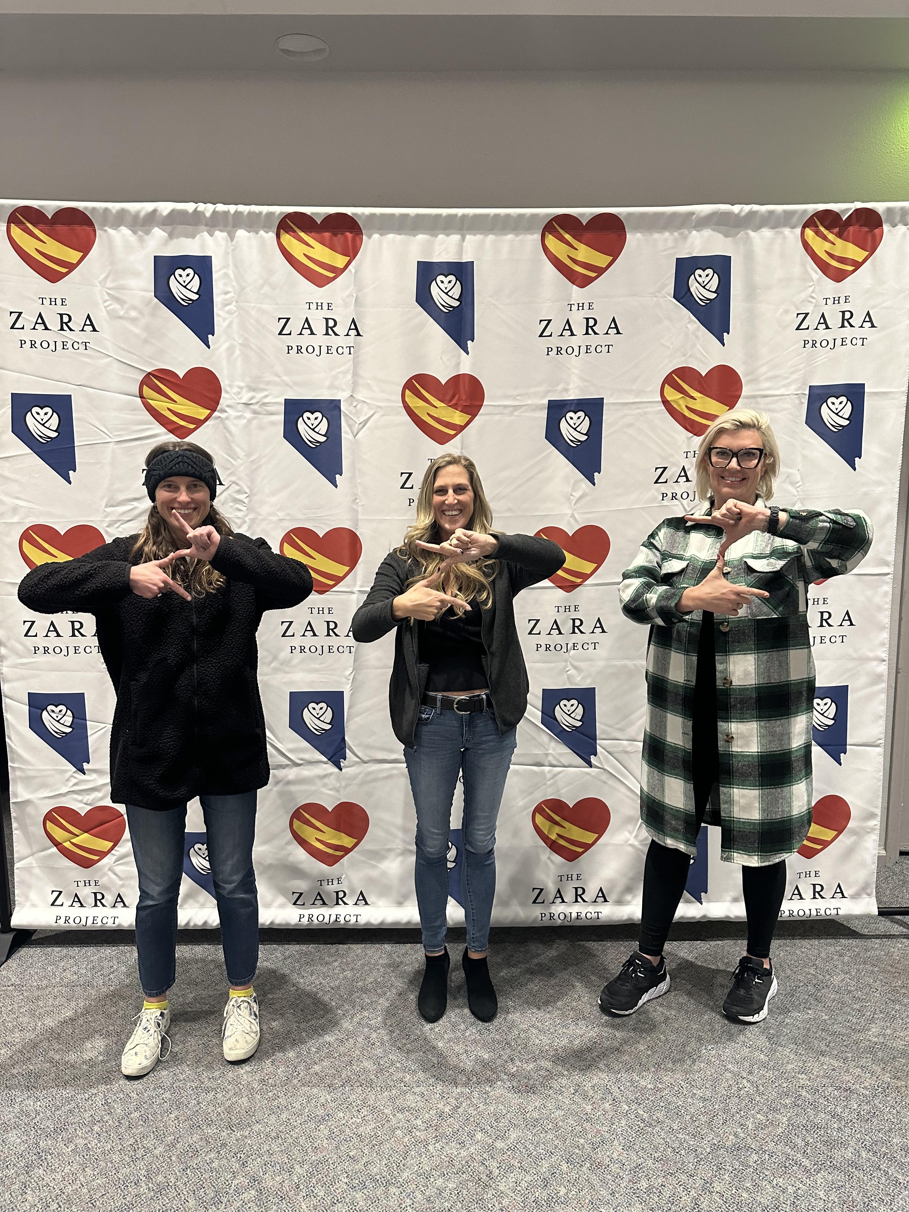 Three Together Tuesdays attendees smiling in front of the Nevada Vax Watch and Zara Project backdrop